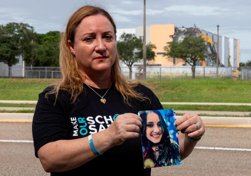 Lori Alhadeff holds a picture of her daughter, Alyssa, as crews use heavy equipment to tear down the 1200 building of Marjory Stoneman Douglas High School on Friday, June 14, 2024, in Parkland, Fla. Alhadeff’s 14-year-old daughter, Alyssa, was among the 17 people who died in the February 14, 2018, mass shooting at the school.