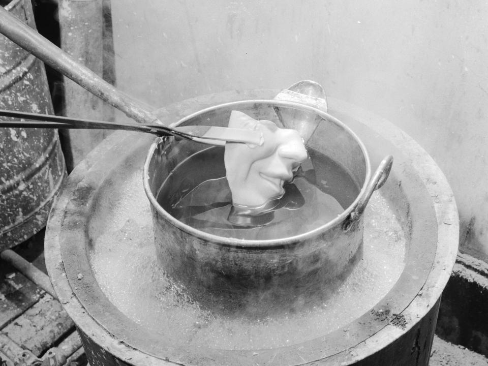 circa 1950: Part of a waxwork's face being lowered in to a melting pot at Madame Tussaud's waxworks museum, London.