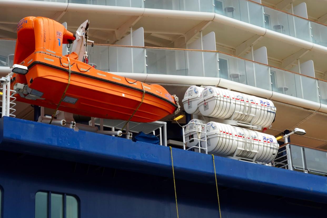 Castries, St Lucia 02 03 2023: Orange rescue boat and white life rafts of cruise passenger vessel with blue hull. There are also windows and balconies of crew and the tourist cabins.