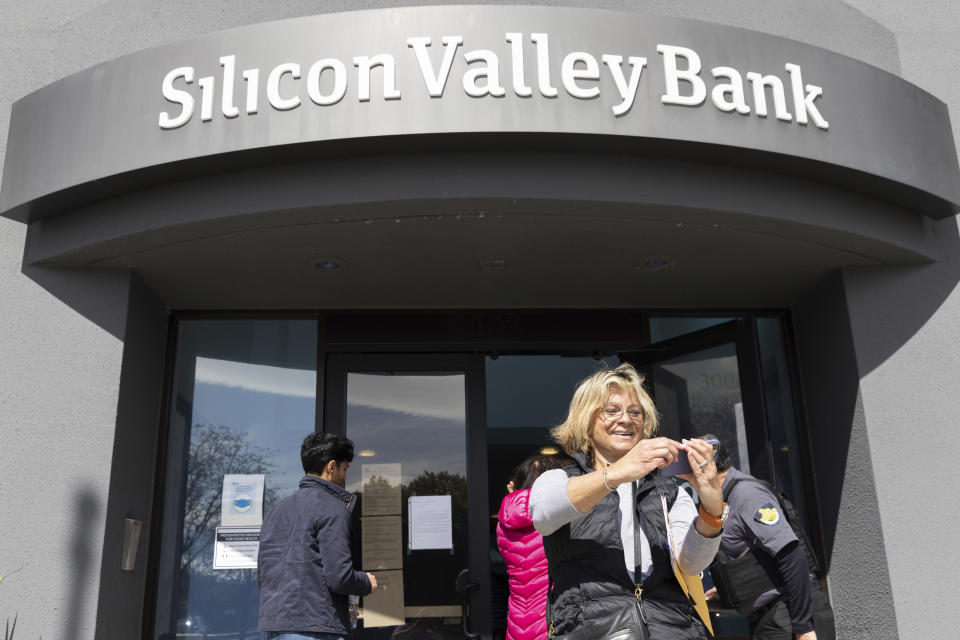 A woman who was part of a line entering the Silicon Valley Bank's headquarters pauses for a selfie in Santa Clara, Calif., on Monday, March 13, 2023. The federal government intervened Sunday to secure funds for depositors to withdraw from Silicon Valley Bank after the banks collapse. Dozens of individuals waited in line outside the bank to withdraw funds. (AP Photo/ Benjamin Fanjoy)