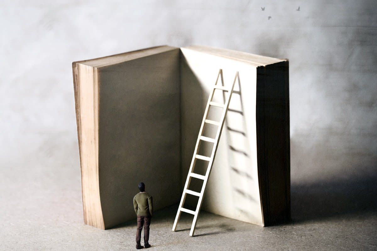 A man looks at an oversized book with a ladder leading up to it. 