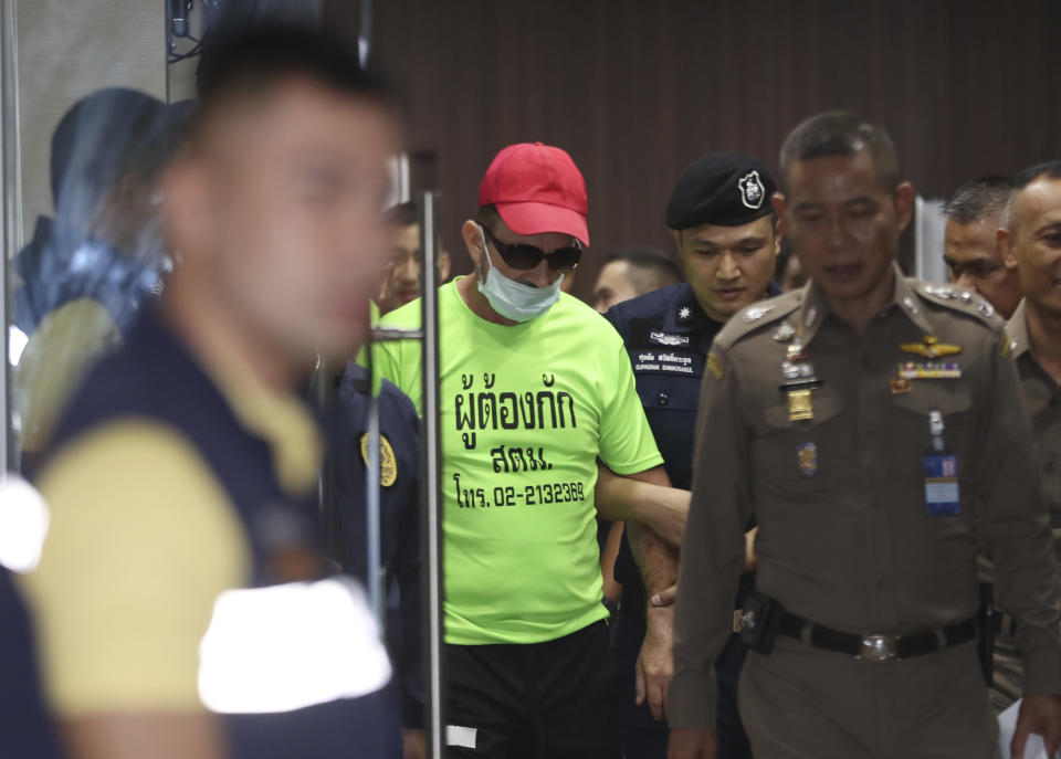 Immigration officers escort Richard Stanislaus, center, at the immigration office in Bangkok, Thailand, Tuesday, Oct. 22, 2019. Police say they are investigating the death of an elderly German woman Margund Schaefer after arresting Stanislaus, also German, for allegedly dumping her body into a canal. (AP Photo/Sakchai Lalit)