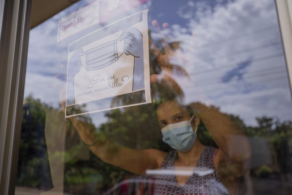 A clothing store worker poses next to a sign encouraging the use of a masks during the COVID-19 pandemic at the entrance to the store in Managua, Nicaragua, Thursday, Sept. 9, 2021. (AP Photo/Miguel Andres)