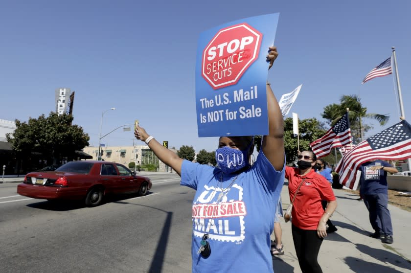 LOS ANGELES, CA - AUGUST 25: Postal employee Toni Givens Lewis waves to cars honking in support during a rally in front of the Beverly Boulevard Bicentennial Station post office in Los Angeles, CA on Tuesday, Aug. 25, 2020 with a message to save the United States Postal Service. (Myung J. Chun / Los Angeles Times)