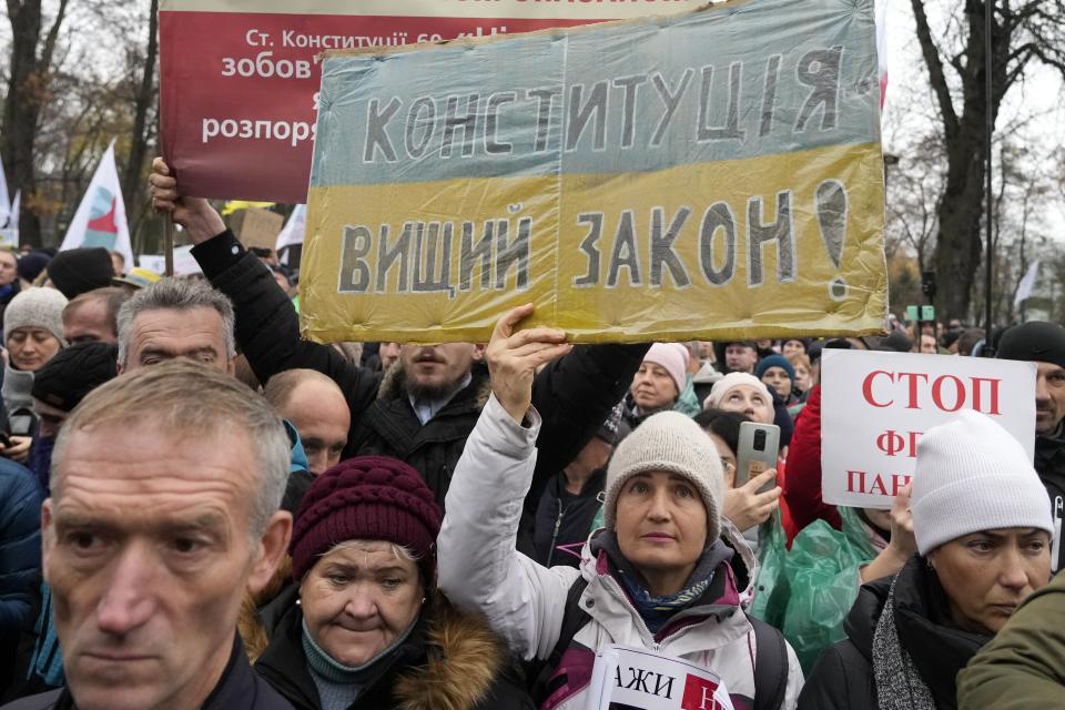 Demonstrators, one holding a poster reading "Constitution is the supreme law", attend a protest against COVID-19 restrictions and vaccine mandates in Kyiv, Ukraine, Wednesday, Nov. 3, 2021. In a bid to stem contagion, Ukrainian authorities have required teachers, government employees and other workers to get fully vaccinated by Nov. 8 or face having their salary payments suspended. In addition, proof of vaccination or a negative test is now required to board planes, trains and long-distance buses. (AP Photo/Efrem Lukatsky)