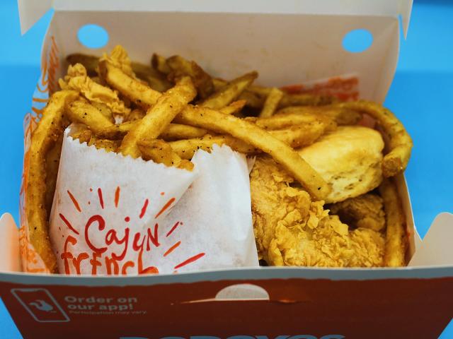 popeyes box of cajun fries chicken tenders biscuit on blue background