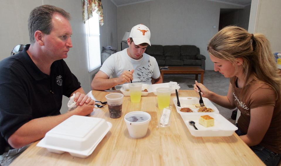 CHALMETTE, LA - MAY 11:  Cabrini High School junior Danielle DiMaggio (R) eats a box dinner with boyfriend Ben Navo (C) and her father David in the temporary trailer where she currently lives in May 11, 2006 in Chalmette, Louisiana. DiMaggio's house was heavily damaged by Hurricane Katrina and she currently lives in a trailer with her father while her mother and brother are still displaced in Lafayette, Louisiana. DiMaggio and every girl at Cabrini High School will be wearing dresses donated by 18-year-old Marissa West from Beltville, Maryland to their prom May 12th. (Photo by Mario Tama/Getty Images)