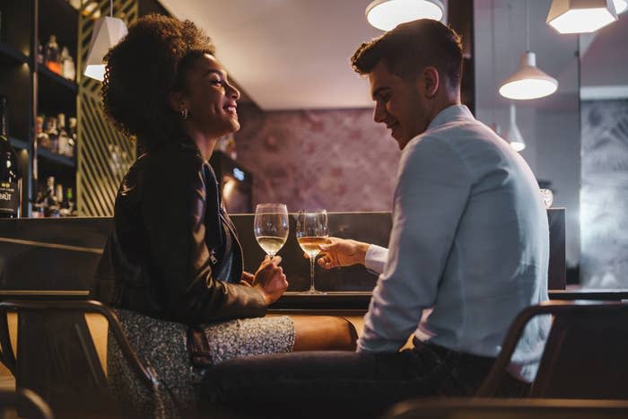 Romantic couple on a date talking holding a glass of white wine sitting at the bar counter in the night