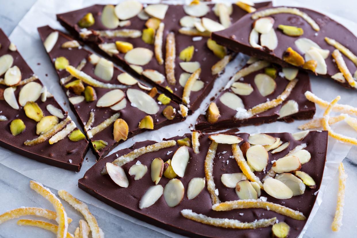 Several pieces of dark chocolate almond bark with sea salt on wax paper with slivers of orange