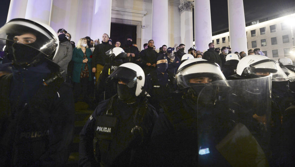 Far-right activists with rosaries sing a religious song as they block entry to a church against hundreds of women's activists and their supporters protesting for the fifth day against a court ruling tightening Poland's strict abortion law, in Warsaw, Poland, on Monday, Oct. 26, 2020. The court said it was unconstitutional to terminate a pregnancy due to fetal congenital defects, effectively banning almost all abortions. (AP Photo/Czarek Sokolowski)