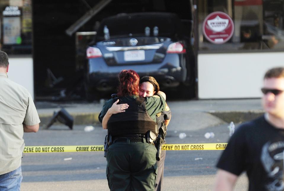 A Sunset Police officer (R), and another law enforcement officer embrace in front of the Sunset Mini Mart where a man drove his vehicle into the store in Sunset, Louisiana, August 26, 2015. A police officer was shot and two people stabbed in a southwest Louisiana town on Wednesday, with a suspect barricading himself in a convenience store, police said. (REUTERS/Leslie Westbrook/The Advocate)