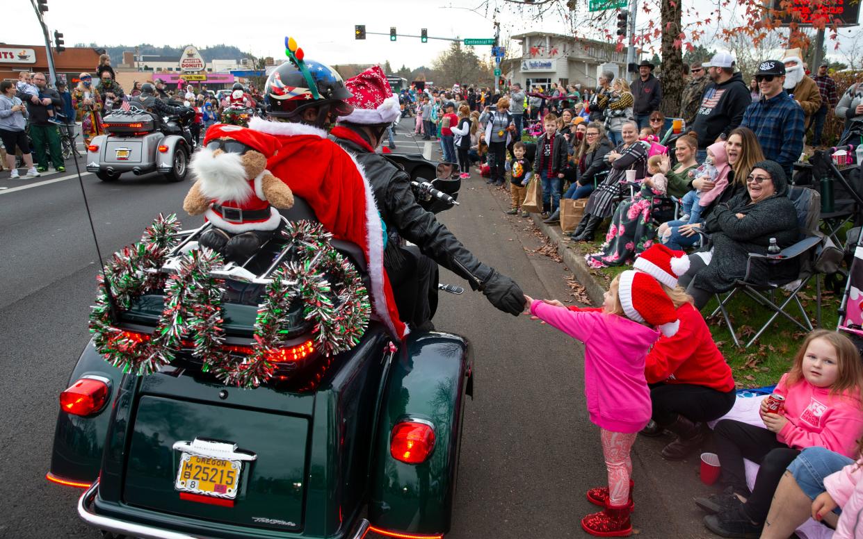 Wanika Dogget, left, and Larry Keeney reach out to two-year-old Ashtyn Pope as they ride in the 2021 Springfield Christmas Parade with their motorcycle group the Willamette Valley Hogs.