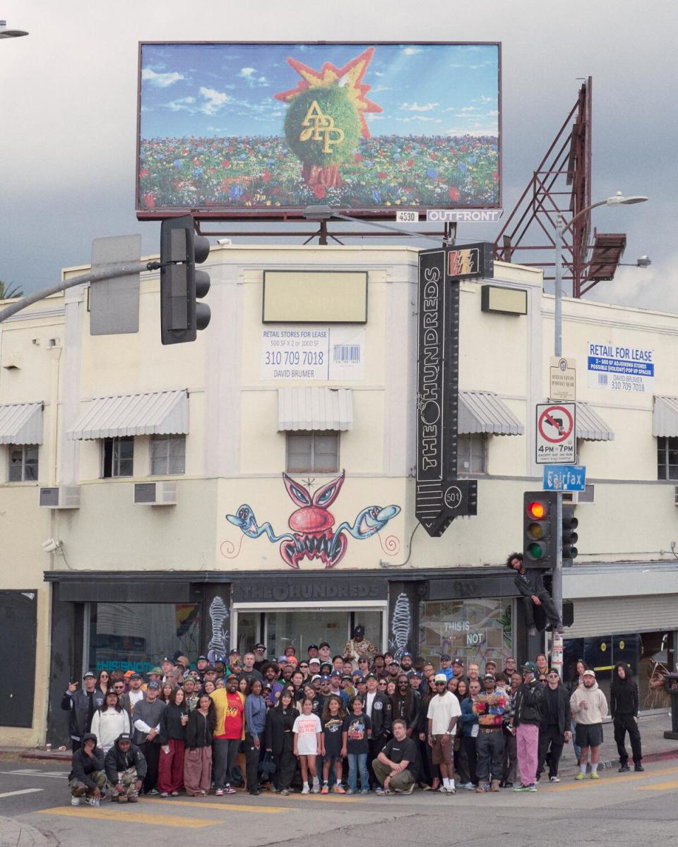 A large group of people poses for a photo outside a store on a corner.