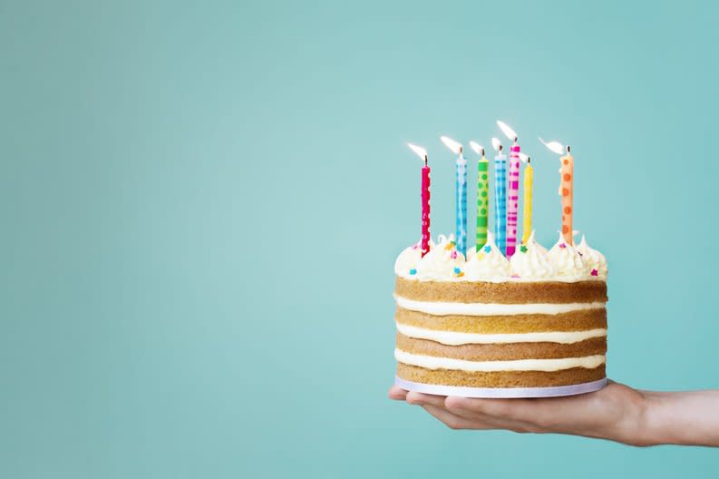 Hand holding a layered vanilla cake with colorful candles