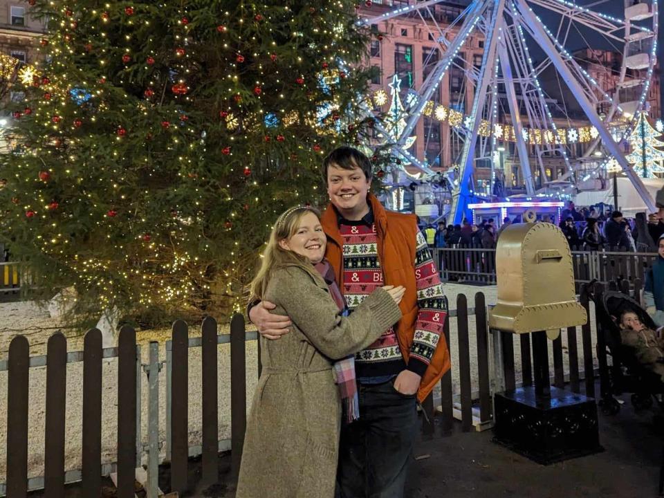mikhaila and scott stand in front of a christmas tree in glasgow