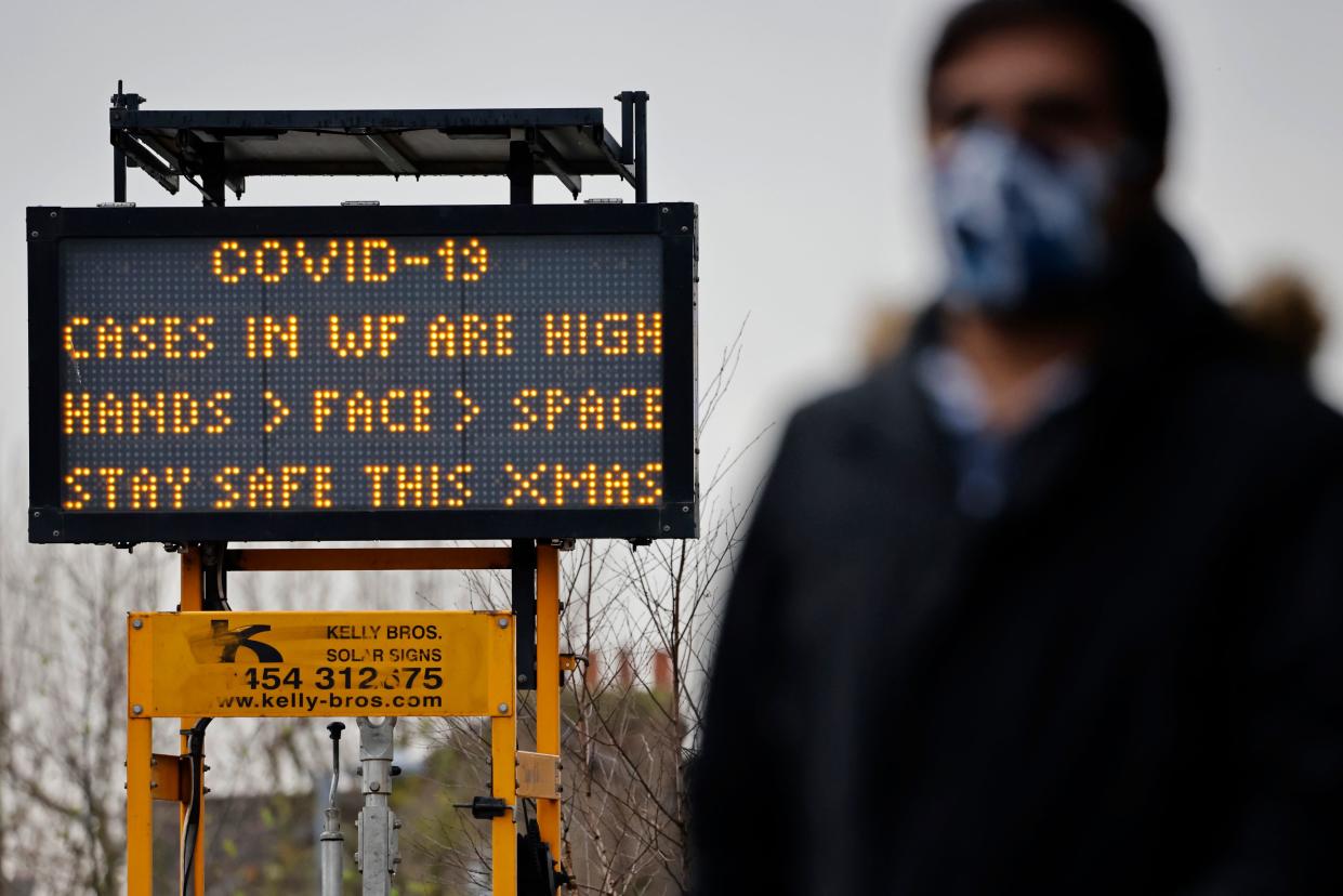 A pedestrian some wearing a face mask or covering due to the COVID-19 pandemic, walks past Coronavirus information signs in Walthamstow in north east London on December 23, 2020. - Britain's public health service urged Prime Minister Boris Johnson on Wednesday to extend the country's Brexit transition period or risk pushing hospitals already struggling with coronavirus "over the edge" in the event of a no-deal departure from the EU single market. (Photo by Tolga Akmen / AFP) (Photo by TOLGA AKMEN/AFP via Getty Images)