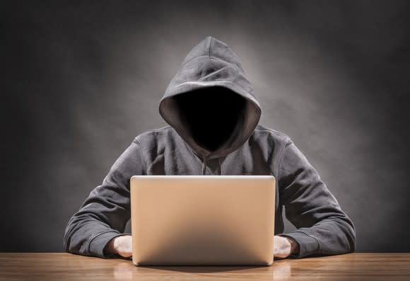 A hacker in a hoodie sitting with a laptop