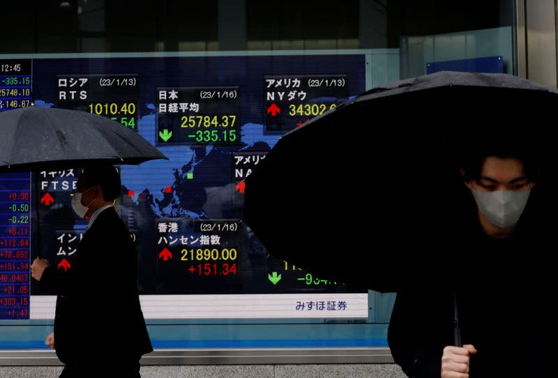 FILE PHOTO: Men walk past an electric board displaying Nikkei and other countries’ indexes outside a brokerage in Tokyo