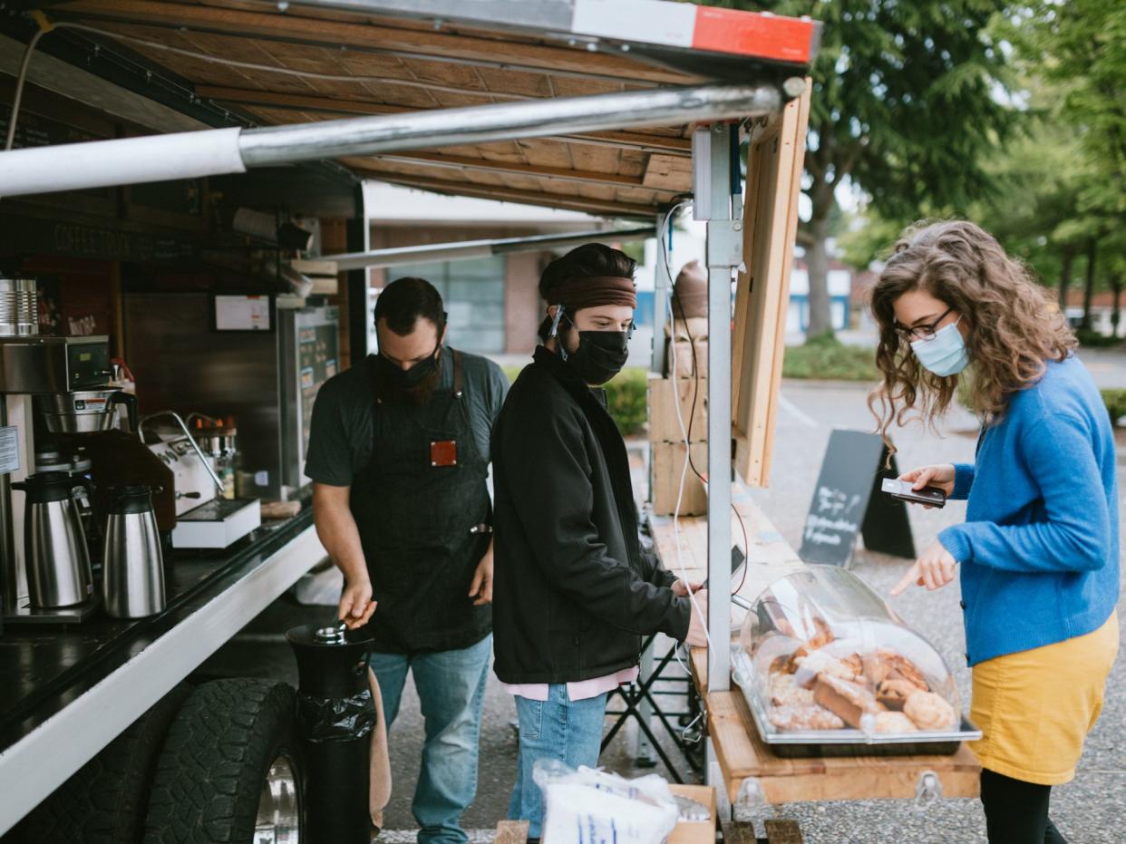 A young man takes the order of a woman at a coffee food cart in the Seattle, Washington area. The outdoor setting is ideal for people to still purchase their coffee and espresso drinks while maintaining social distance during the Coronavirus pandemic.