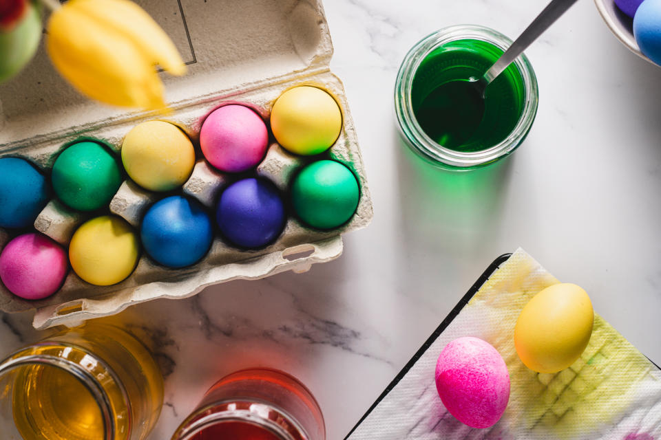 Easter eggs dyed in various colors in a carton, with cups of dye and a paintbrush nearby