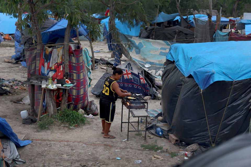 A man cooks food on a grill in the middle of several large tents.