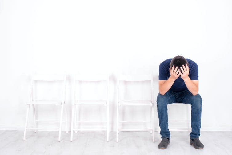 Young man sits alone on a chair in a waiting room.