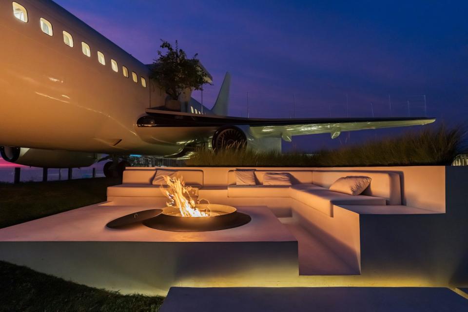 A white couch and firepit sit next to a plane at night.