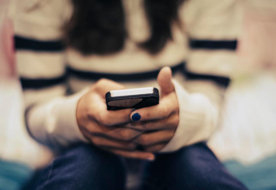 A person seated with legs crossed, texting on a smartphone