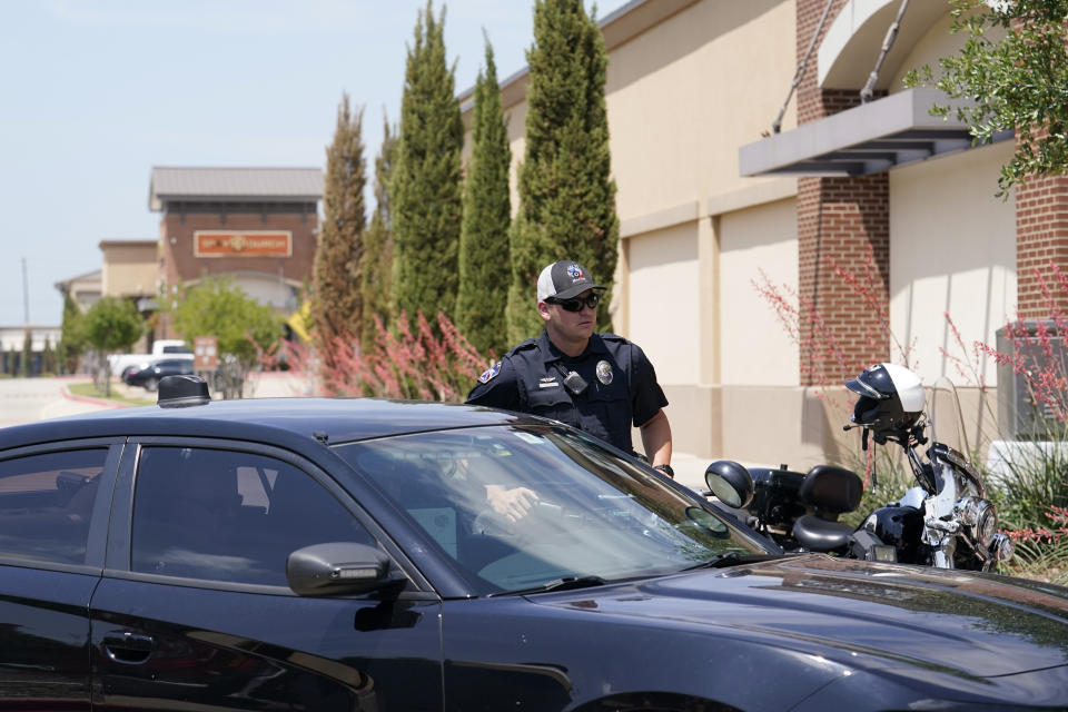 A city of Allen, Texas, police officer stands by another, sitting in a vehicle, by closed entrances to a mall where several people were killed several days earlier, Monday, May 8, 2023, in Allen, Texas. (AP Photo/Tony Gutierrez)