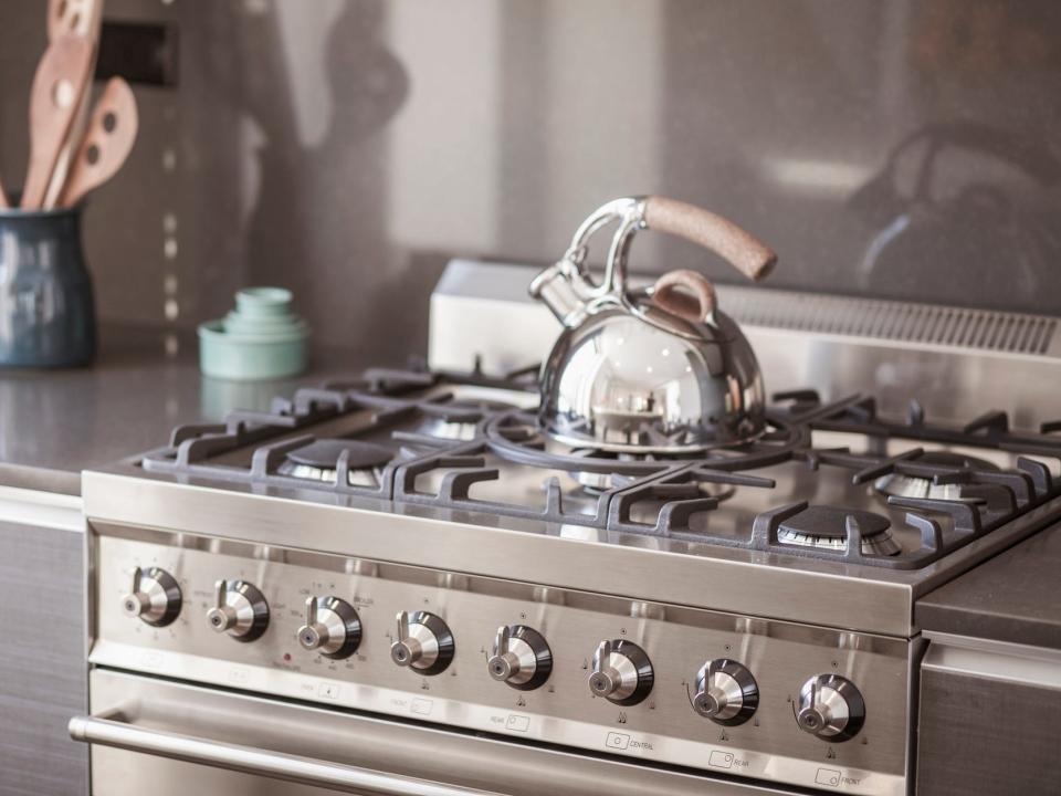 A stainless-steel stovetop range with a silver kettle and canister of wooden spoons on counter in the background