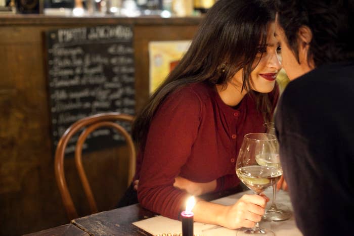 A woman and a man smile intimately at a candlelit table in a restaurant with a chalkboard menu in the background