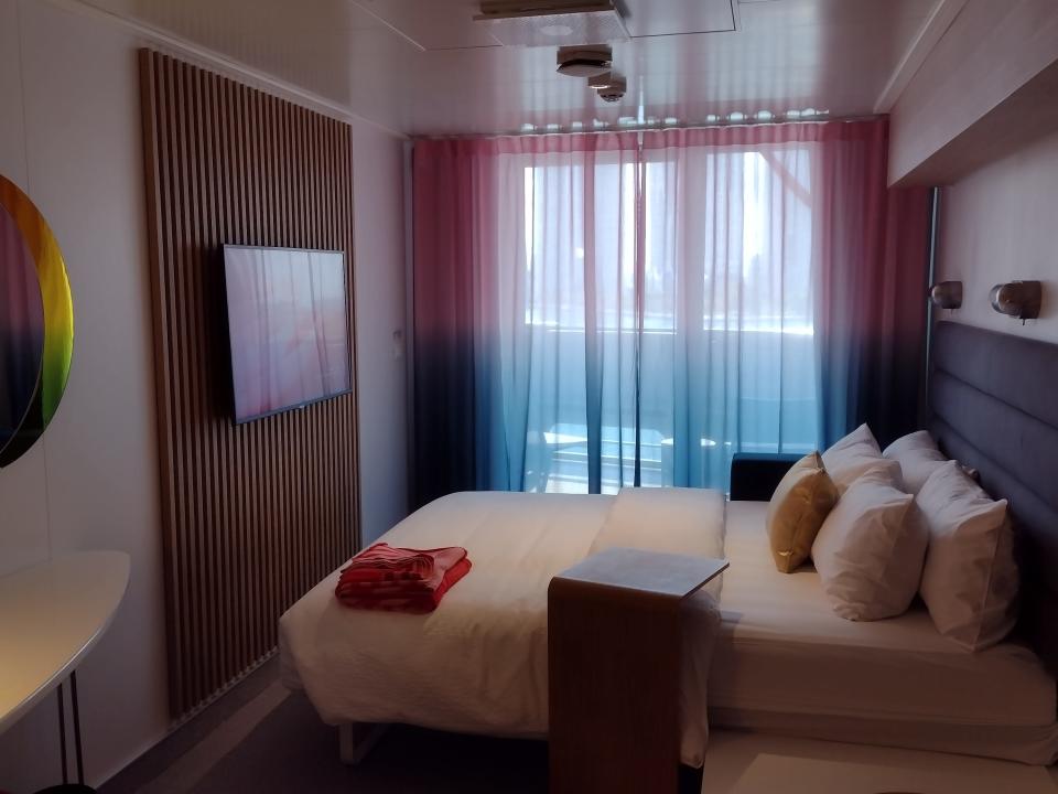 A cruise ship cabin with one bed and a balcony.