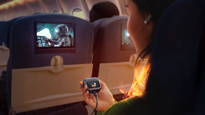 A person holds an earbud charging case that's connected to an in-flight entertainment system.