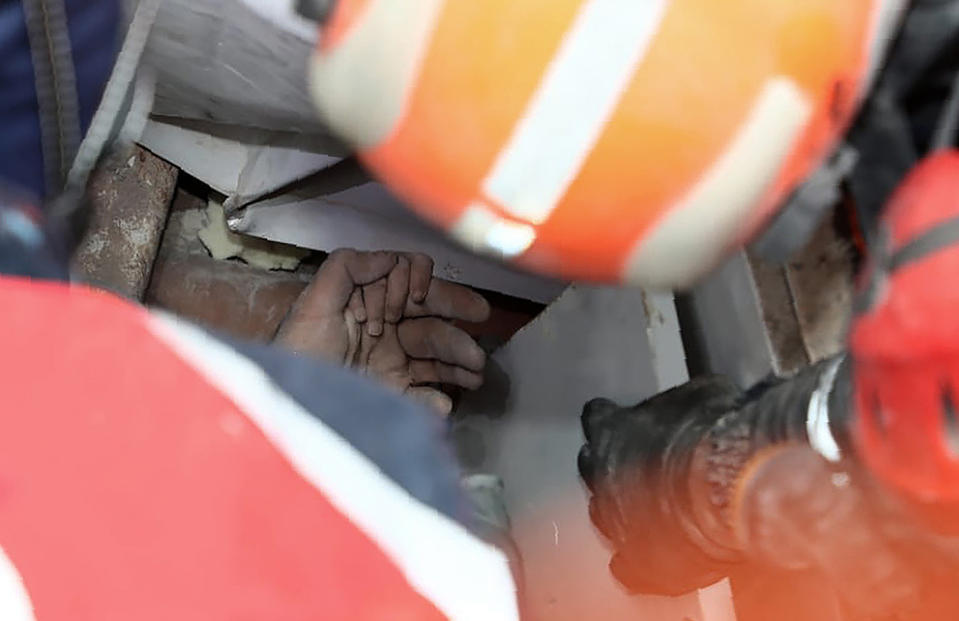 In this photo provided by the government's Disaster and Emergency Management Agency, a rescue worker holds Ayda Gezgin by the hand in the rubble of a collapsed apartment building in the Turkish coastal city of Izmir, Turkey, Tuesday, Nov. 3, 2020, after they discovered the young girl alive, four days after a strong earthquake hit Turkey and Greece. The girl, Ayda Gezgin, was seen being taken into an ambulance on Tuesday, wrapped in a thermal blanket, amid the sound of cheers and applause from rescue workers. (AFAD via AP)