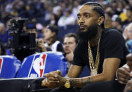 FILE - In this March 29, 2018, file photo, rapper Nipsey Hussle watches an NBA basketball game between the Golden State Warriors and the Milwaukee Bucks in Oakland, Calif. Hussle has been shot and killed outside his Los Angeles clothing store, Los Angeles Mayor Eric Garcetti said March 31, 2019. He was 33. (AP Photo/Marcio Jose Sanchez, File)