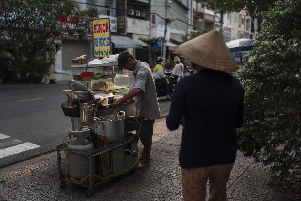 Pham Van Sang, a street food vendor and migrant from the Mekong Delta, prepares a noodle dish for a customer as his wife, Luong Thi Ut, carries a tray in Ho Chi Minh City, Vietnam, Monday, Jan. 22, 2024. The couple works in the city's industrial zone, a common destination for many migrants from the Mekong Delta in search of a better life. (AP Photo/Jae C. Hong)