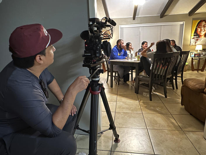 This image released by ABC News shows Nicco Quiñones filming inside the home of Jerry and Veronica Mata. Their daughter Tess, pictured on the wall, was one of 19 elementary school students shot and killed in Uvalde, Texas, last May. For a year, ABC News kept a team in Uvalde. The result is a nuanced portrait of what happens over time to a suffering community, as seen in the two-hour documentary, “It Happened Here — A Year in Uvalde,” that airs first Friday on ABC and Saturday on Hulu. (Jenny Wagnon Courts/ABC News via AP)