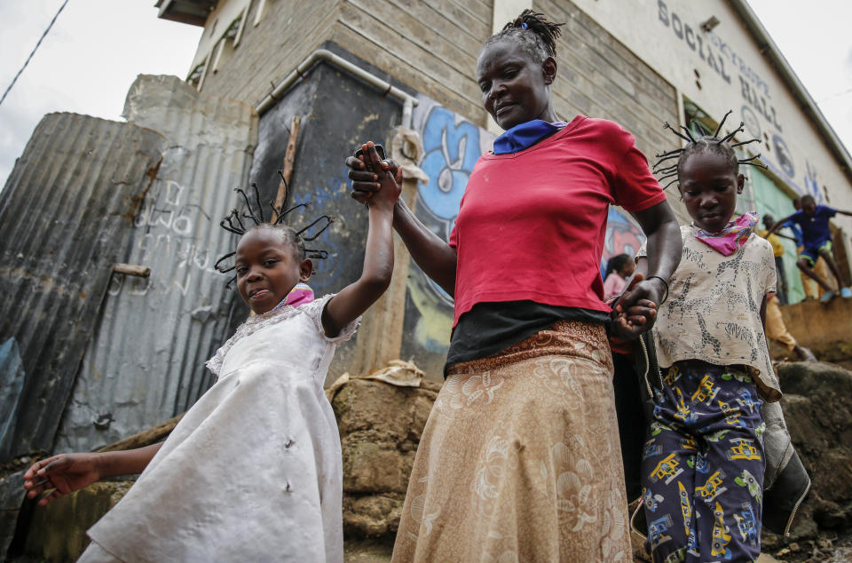 FILE - In this Sunday, May 3, 2020 file photo, Margaret Andeya takes her daughter Gettrueth Ambio, 12, right, and her neighbor's daughter Jane Mbone, 7, left, back home after having their hair styled in the shape of the new coronavirus at the Mama Brayo Beauty Salon in the Kibera slum, or informal settlement, of Nairobi, Kenya Sunday, May 3, 2020. The coronavirus has revived a hairstyle in East Africa, one with braided spikes that echo the virus' distinctive shape, with the growing popularity in part due to economic hardships linked to virus restrictions. (AP Photo/Brian Inganga, File)