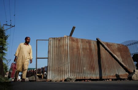A Kashmiri man walks past a blockade put up by residents to prevent Indian security force personnel from entering their neighborhood during restrictions, in Srinagar