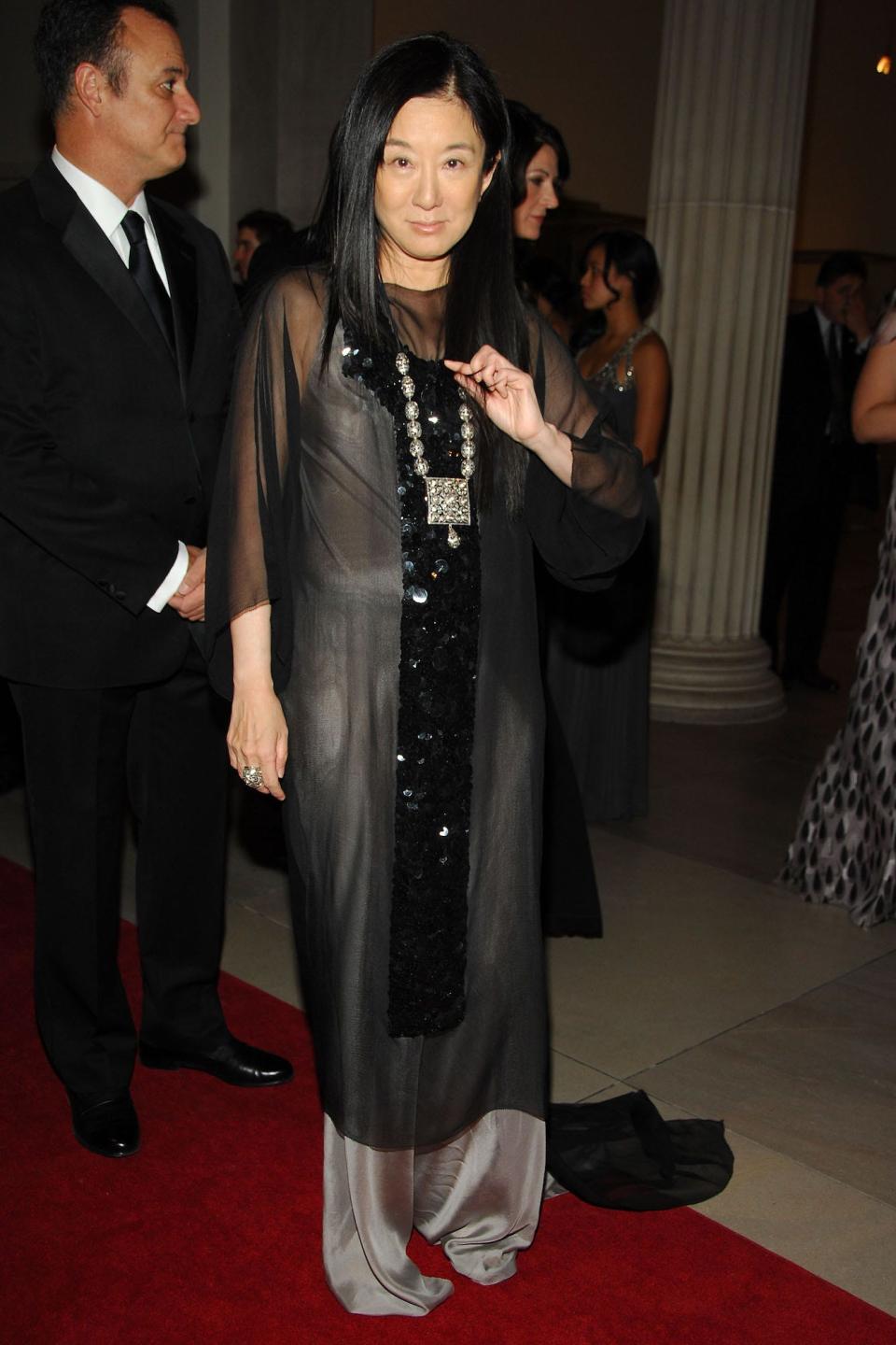 Vera Wang stands on the red carpet at the 2007 Met Gala, wearing a loose gray silk dress, with a black, sheer piece overtop.