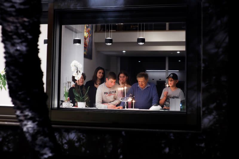 Israeli Holocaust survivor Avraham Harshalom, 95, is seen together with his family through a window as they light a hanukkiyah, a candlestick with nine branches that is lit to mark Hanukkah, the 8-day Jewish Festival of Lights, in Ramat Gan, Israel