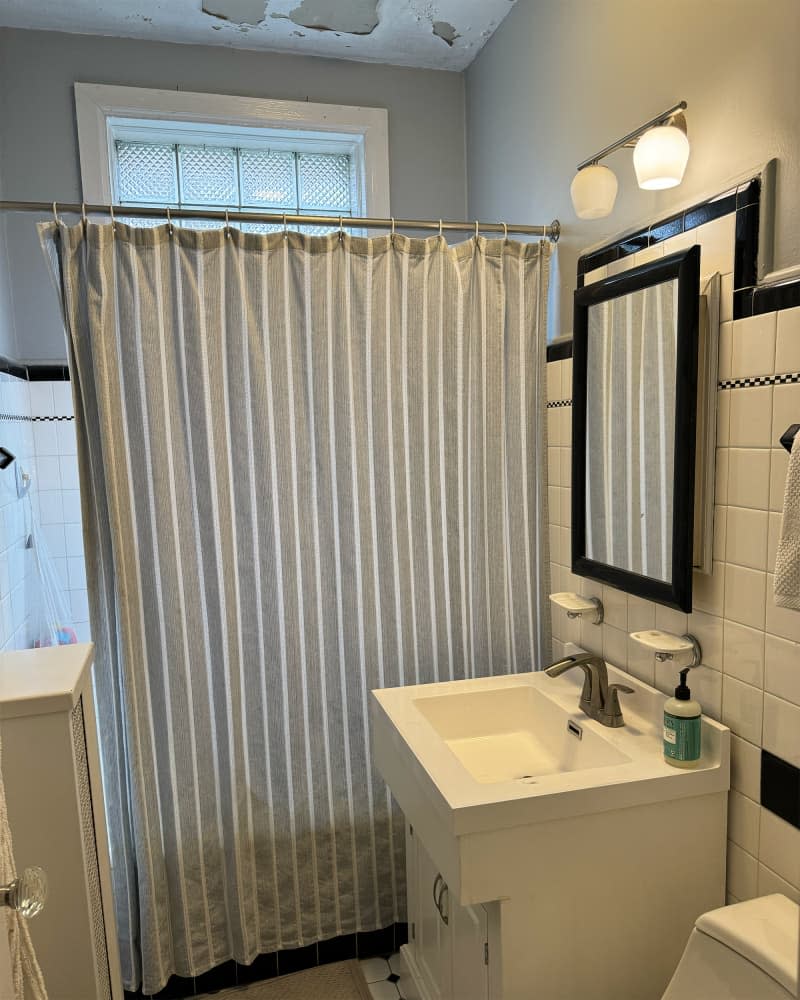 Striped shower curtain in black and white bathroom before renovation.