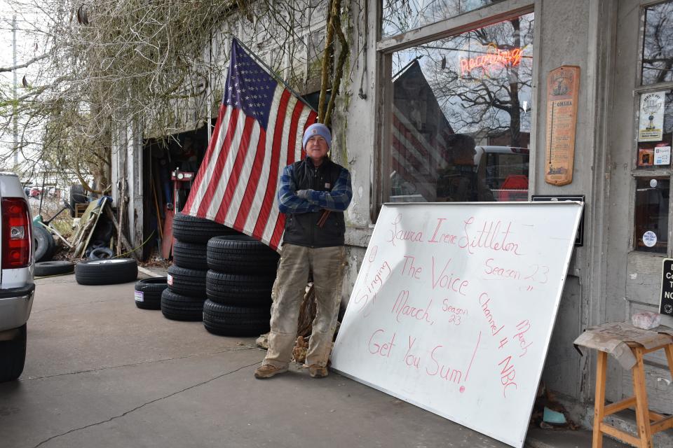 Bill Littleton posing in front of his style of social media at his shop, Bill's Tires in Downtown Dickson. The sign is promoting his daughter Laura's performance on 'The Voice.'