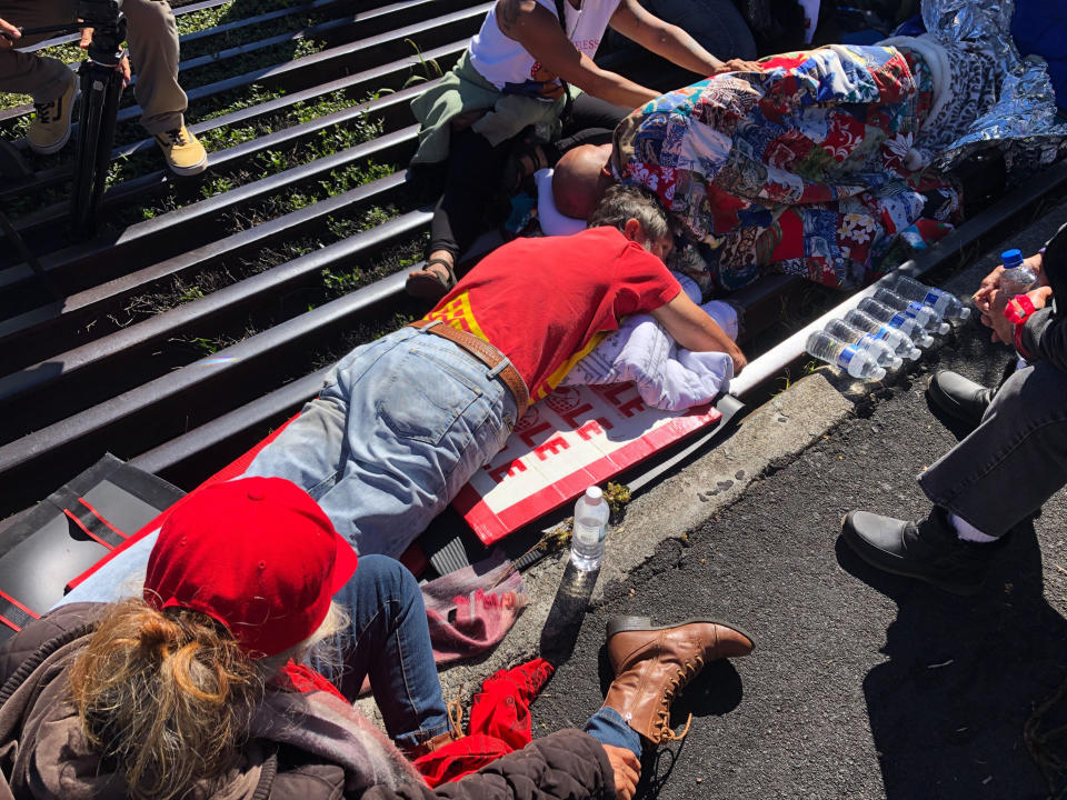 Activist Walter Ritte, left, and others lay chained to a cattle grate blocking a road at the base of Hawaii's tallest mountain, Monday, July 15, 2019, in Mauna Kea, Hawaii, protesting the construction of a giant telescope on land that some Native Hawaiians consider sacred. (AP Photo/Caleb Jones)