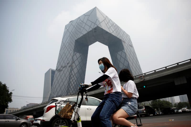 Woman wearing a face mask rides past the CCTV headquarters in Beijing