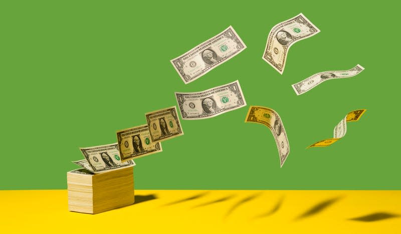 Stack of US $1 bills with bills flying away on yellow shelf, green background - Photo: PM Images (Getty Images)