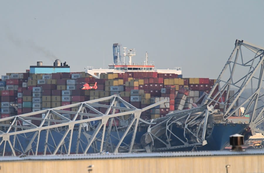 The steel frame of the Francis Scott Key Bridge sits on top of a container ship as a helicopter makes a pass after the bridge collapsed in Baltimore, Maryland, on March 26, 2024. The bridge collapsed after being struck by a container ship, sending multiple vehicles and up to 20 people plunging into the harbor below. “Unfortunately, we understand that there were up to 20 individuals who may be in the Patapsco River right now as well as multiple vehicles,” Kevin Cartwright of the Baltimore Fire Department told CNN. Ship monitoring website MarineTraffic showed a Singapore-flagged container ship called the Dali stopped under the bridge. (Photo by ROBERTO SCHMIDT / AFP) (Photo by ROBERTO SCHMIDT/AFP via Getty Images)