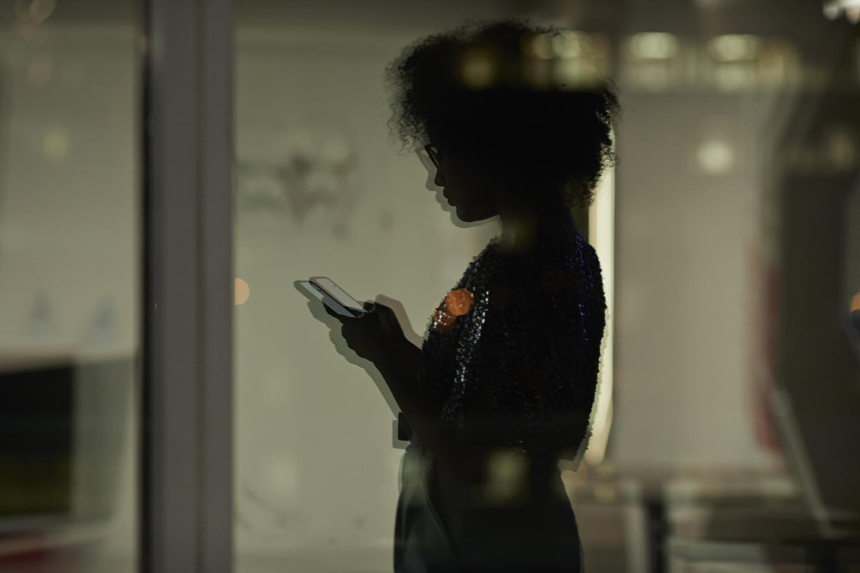 Reflection of young businesswoman checking smartphone in the office at night (Klaus Vedfelt / Getty Images)