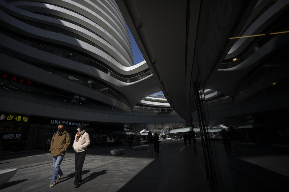 People wearing face masks walk through a shopping and office complex in Beijing, Wednesday, March 1, 2023. (AP Photo/Mark Schiefelbein)