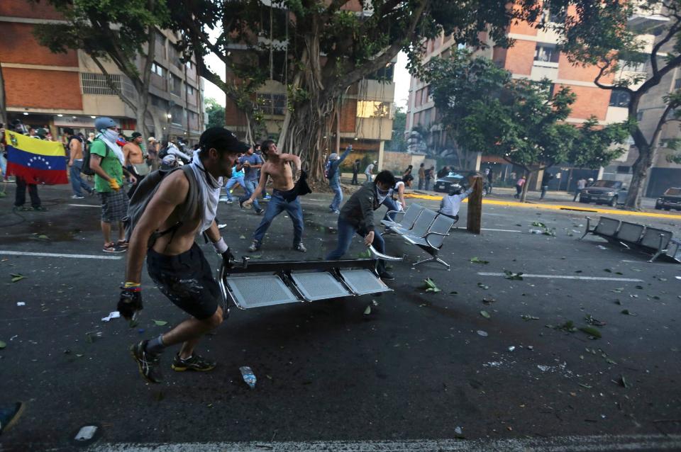 Demonstrators block a road with chairs as others throw stones at National Bolivarian Police (BNP) in Caracas, Venezuela, Saturday, Feb. 15, 2014. Venezuelan security forces backed by water tanks, tear gas and rubber bullets dispersed groups of anti-government demonstrators who tried to block Caracas' main highway Saturday evening. (AP Photo/Fernando Llano)